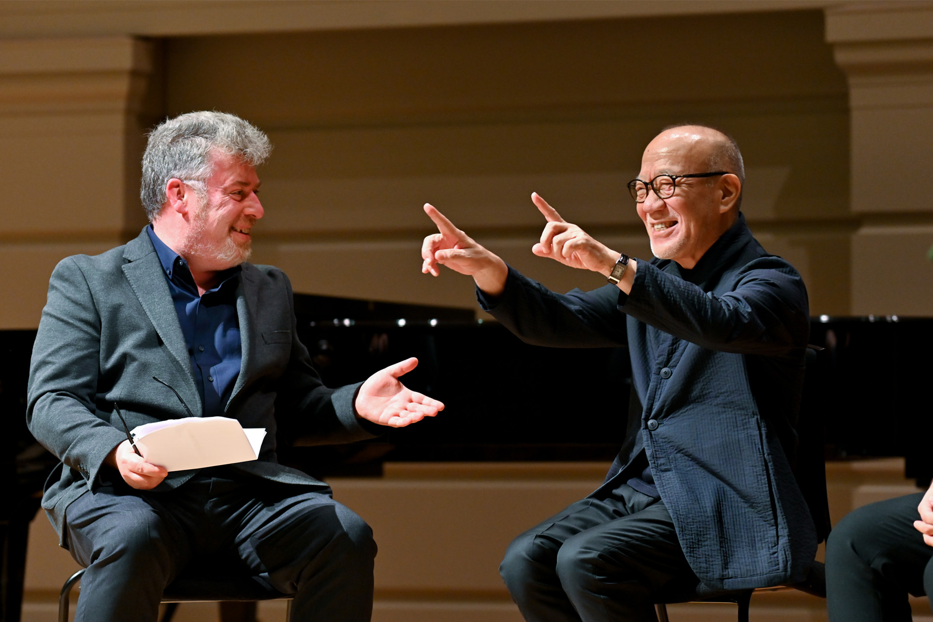 Two men on stage, wearing smart suits, talking on stage.